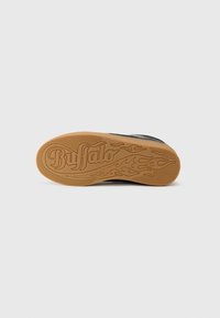 Sola de sapatilha preta com uma superfície texturada e uma sola de borracha castanha com a palavra "Buffalo" e padrões de chamas.