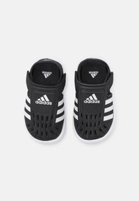 Black Adidas slip-on shoes with white accents, featuring a perforated design and three white stripes on each side, made from lightweight material.