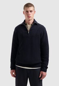 Marineblauw geribbeld sweater met een kwart rits en een hoge kraag, voorzien van een contrasterende binnenlaag die zichtbaar is bij de hals. Heeft een losse pasvorm.