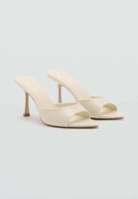 Mule beige a punta aperta con una parte superiore in sintetico liscia, ampia fascetta anteriore incrociata e un tacco sottile. Design minimalista con una leggera texture.