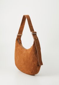 Borsa a spalla in suede marrone con una forma morbida, ampia tracolla regolabile e accessori in argento. Presenta una tasca con cerniera lungo la parte superiore.