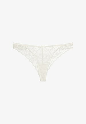 Spitzen-Tanga in Elfenbein mit floralen Mustern, gewellten Kanten und einer kleinen Schleife in der Mitte. Leichter, zarter Stoff für optimalen Komfort.