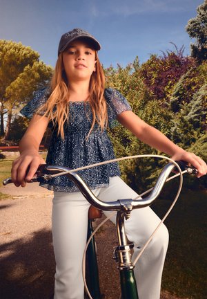 Ein junges Mädchen mit einer Kappe fährt auf einem grünen Fahrrad einen sonnigen Weg entlang, umgeben von Bäumen und Büschen in einem Park.