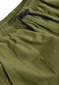 Olivenfarvede shorts med elastisk talje, udstyret med en sort snøre og en glat tekstur med subtil glans.