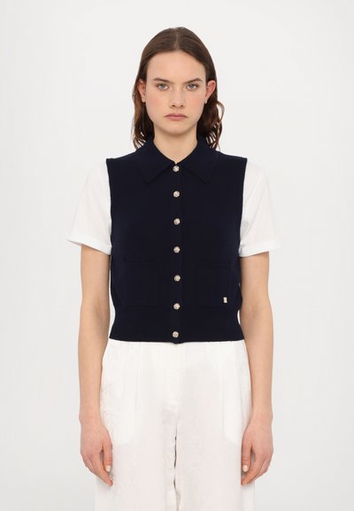 Marinblå strikket ærmeløs cardigan med krave, sølvfarvet knaplukning, to frontlommer og et lille logo-accents.