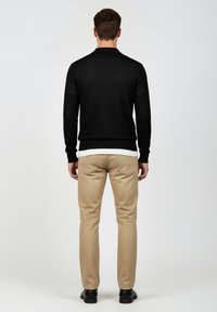 Maglione nero lavorato a maglia, pantaloni beige e scarpe nere. Il maglione presenta una scollatura rotonda e polsini a costine. I pantaloni sono a gamba dritta con tasche.