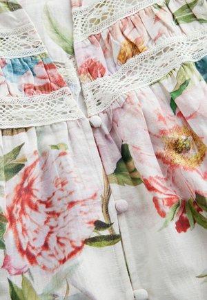 Blouse florale en tissu léger avec des motifs de pivoines roses et rouges, bordure en dentelle et détails de boutons sur le devant.