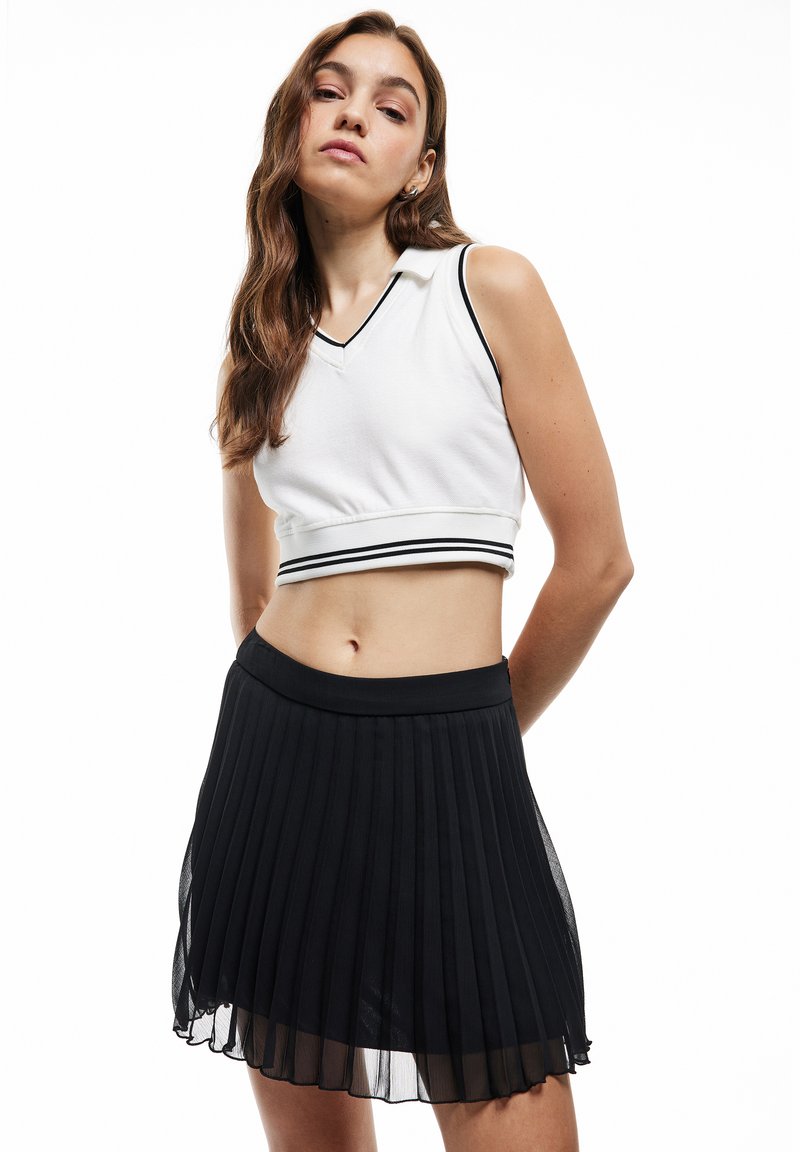 Valkoinen lyhyt toppi, jossa on V-niska ja mustat raidat, yhdistettynä mustaan, kevyeen, laskostettuun mini-hameeseen.