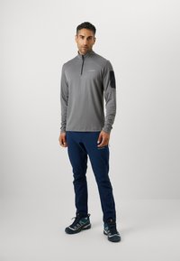 Grå langermet genser med glidelås i halsen, svart skulderpanel; sammen med blå bukser og gråblå joggesko med forsterkede såler.