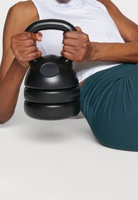 Kettlebell noir au design arrondi, poignée texturée et corps lisse, tenu à deux mains, posé sur un fond clair.