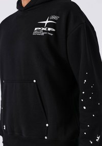 Zwarte hoodie van zachte stof met een frontzak, wit logo op de borst, zilveren drukknoopdetails en een gestructureerd gespikkeld patroon op de mouw.