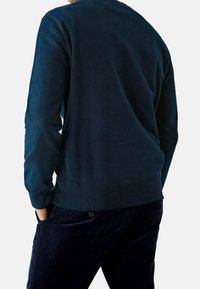 Felpa blu navy realizzata in tessuto morbido, con maniche lunghe, scollatura rotonda e polsini a costine. Abbinate a pantaloni di velluto a coste scuri.