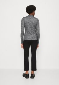 Haut ajusté à manches longues en maille texturée bleu marine et blanche, avec un col montant. Associé à un pantalon noir droit et des chaussures noires épaisses.