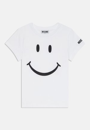 Bílé dětské tričko s krátkým rukávem s černým grafickým smajlíkem na přední straně a textem "Moschino" na štítku za krkem a na levém rukávu.