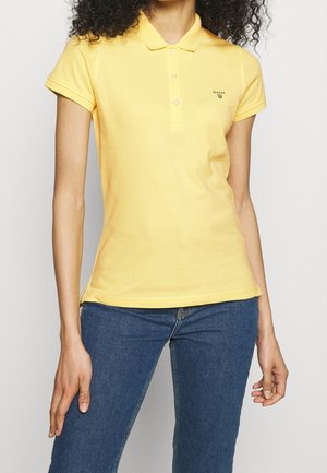 Polo giallo con maniche corte, colletto e patta con tre bottoni. Presenta un piccolo logo sul lato sinistro del petto.