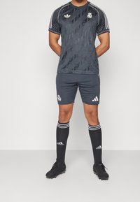 Completo da calcio nero con una maglia a fantasia, pantaloni abbinati, calze nere con strisce bianche e scarpe nere. Loghi visibili sulla maglia e sui pantaloni.