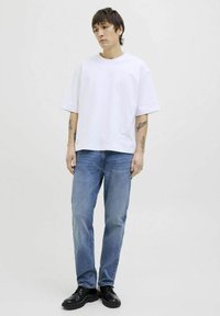 Camiseta blanca de manga corta y corte relajado, combinada con jeans de mezclilla azul claro. El modelo lleva zapatos negros de cordones. Un atuendo simple y casual.