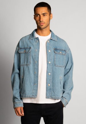 Giacca in denim azzurro chiaro con chiusura a bottoni, due tasche sul petto e vestibilità ampia. Presenta dettagli cuciti e bottoni metallici.