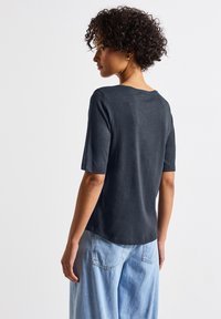 Ciemnoszara koszulka z krótkim rękawem i okrągłym dekoltem, miękka w dotyku, o luźnym kroju, w zestawie z jasnoniebieskimi spodniami o szerokich nogawkach.