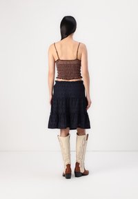 Barna smockolt cropped top, sötétkék gyöngyökkel díszített szoknya fodrokkal, és magas krémszínű cowboy csizma barna díszítéssel. Sima textúrák és réteges kialakítás.