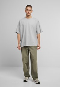Camiseta gris de gran tamaño con hombros caídos, combinada con pantalones rectos de color verde oliva. Diseño minimalista; la tela parece suave y texturizada.