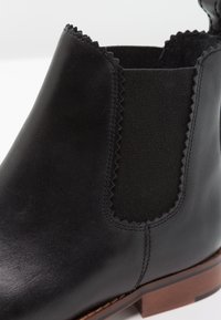 Bottine en cuir noir avec panneau latéral élastique et détail à bord festonné, dotée d'un petit talon empilé marron.