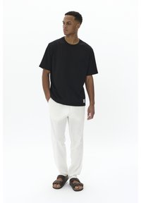 Juoda trumpomis rankovėmis marškinėliai, laisvo kirpimo, derinami su baltomis lininėmis kelnėmis ir rudos spalvos sandalais. Paprastas dizainas be matomų raštų ar logotipų.