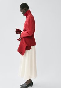 Rode jas met kraag en een getailleerde taille, gecombineerd met een vloeiende witte rok. Zwarte schoenen maken de outfit compleet. Eenvoudig, gestructureerd ontwerp.