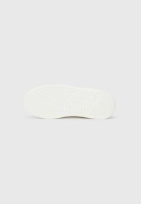 Suola di scarpa in gomma bianca con superficie texture, caratterizzata da un grip a motivi e aree lisce, progettata per offrire aderenza e flessibilità.