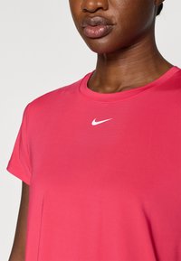 Camiseta de manga corta y cuello redondo en tela de color rosa brillante con una textura suave y un pequeño logo blanco de Nike en el pecho.