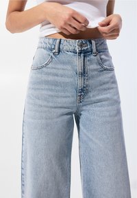 Světle modré džíny s vysokým pasem vyrobené z denimu, s rovnými nohavicemi, pěti kapsami a kontrastním šitím s knopkovým zapínáním.