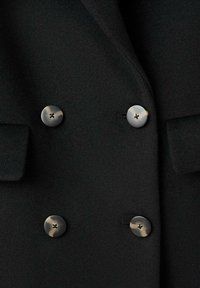 Czarna tkanina wełnianego płaszcza z dwurzędowym fasonem, czterema okrągłymi guzikami w ciemnym metalicznym kolorze oraz dwoma kieszeniami z patkami.