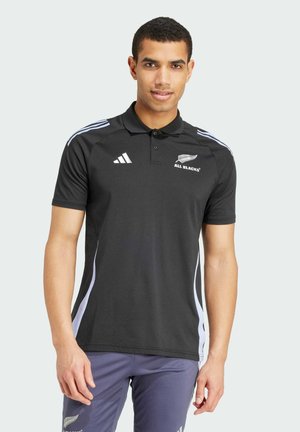 Svart polo t-shirt med vita sidostripes, med krage och "ALL BLACKS" logga. Tillverkad av mjukt, fukttransporterande tyg.