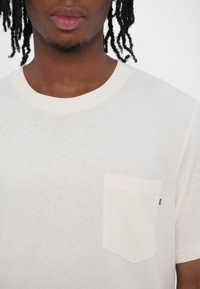 Krämfärgad bomulls t-shirt med rund halsringning, kort ärm och pocket på vänster bröst. Minimalistisk design med en subtil textur.