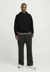 Schwarzer Hoodie mit einer Fronttasche und einer grauen Innenschicht, kombiniert mit locker sitzenden dunkelgrauen Hosen und silbernen Sportschuhen.