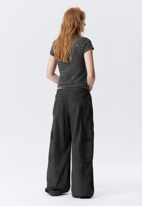 Pantalons cargo noirs �à jambes larges, dotés de plusieurs poches, associés à un t-shirt ajusté noir et blanc à rayures. Texture de tissu lisse.