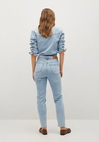 Camisa de denim azul claro con mangas arremangadas, combinada con jeans skinny azul claro. El conjunto incluye un cinturón de cuero marrón y unos sencillos zapatos marrones.
