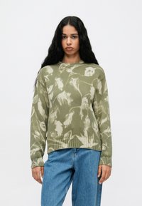 Kelių žalios spalvos megztinis su baltu gėlių raštu, su įribiavimais ir laisvu siluetu. Derinamas su laisvomis mėlynomis džinsų kelnėmis.