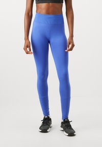 Blå atletiska leggings i elastisk väv med hög midja. Har en mjuk yta och helängdsdesign. Bärs med svarta sneakers.