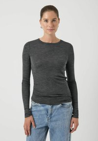 Dopasowany ciemnoszary top z długim rękawem i zaokrąglonym dekoltem o gładkiej fakturze, zestawiony z jasnoniebieskimi, wysokim stanem jeansami.