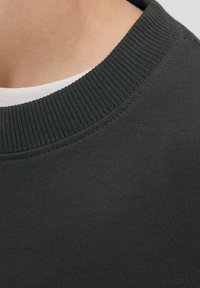 Felpa grigia scura con collo a coste, che mostra una texture del tessuto liscia e un sottile strato bianco sotto al colletto.