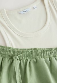 Cremefarvet ribbet tanktop og grønne shorts med elastisk talje og bindedetalje, der viser en glat tekstur og en afslappet pasform. Mærket synligt.