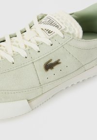 Zapatillas de ante verde claro de Lacoste con cordones blancos, lengüeta de malla y logo de cocodrilo metálico en el lateral.