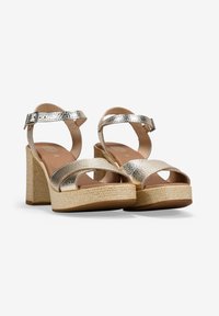 Sandalias de tacón plateadas metálicas con tira de tobillo, plataforma de yute trenzado y un diseño de tiras cruzadas anchas. Material texturizado y tacón resistente.