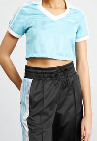 Person som bär en ljusblå Adidas kortärmad träningsskjorta och svarta träningsbyxor med vit-blåa ränder på sidorna.