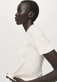 Pleteni srajčni majica s kratkimi rokavi iz mehke bele tkanine, oprijet kroj, gladka tekstura, čiste linije in subtilni detajli ob šivih.