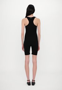 Module sans manches noir avec un design ajusté, atteignant le milieu de la cuisse. Texture lisse, peu de détails et un col rond.