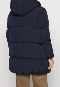 Námořnicky modrá prošívaná péřová bunda s kapucí, elastickými manžetami a hladkým, texturovaným povrchem. Vhodná pro nošení za chladného počasí.