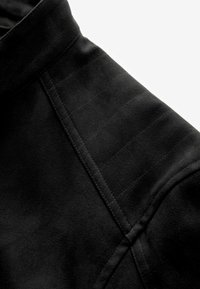 Black faux suede jacket section with a high collar, featuring subtle stitching details and a smooth texture. Close-up on shoulder area.