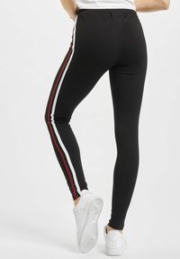 Sort leggings med høj talje, som har lodrette striber i hvidt og rødt langs hver side. Båret med hvide sneakers.